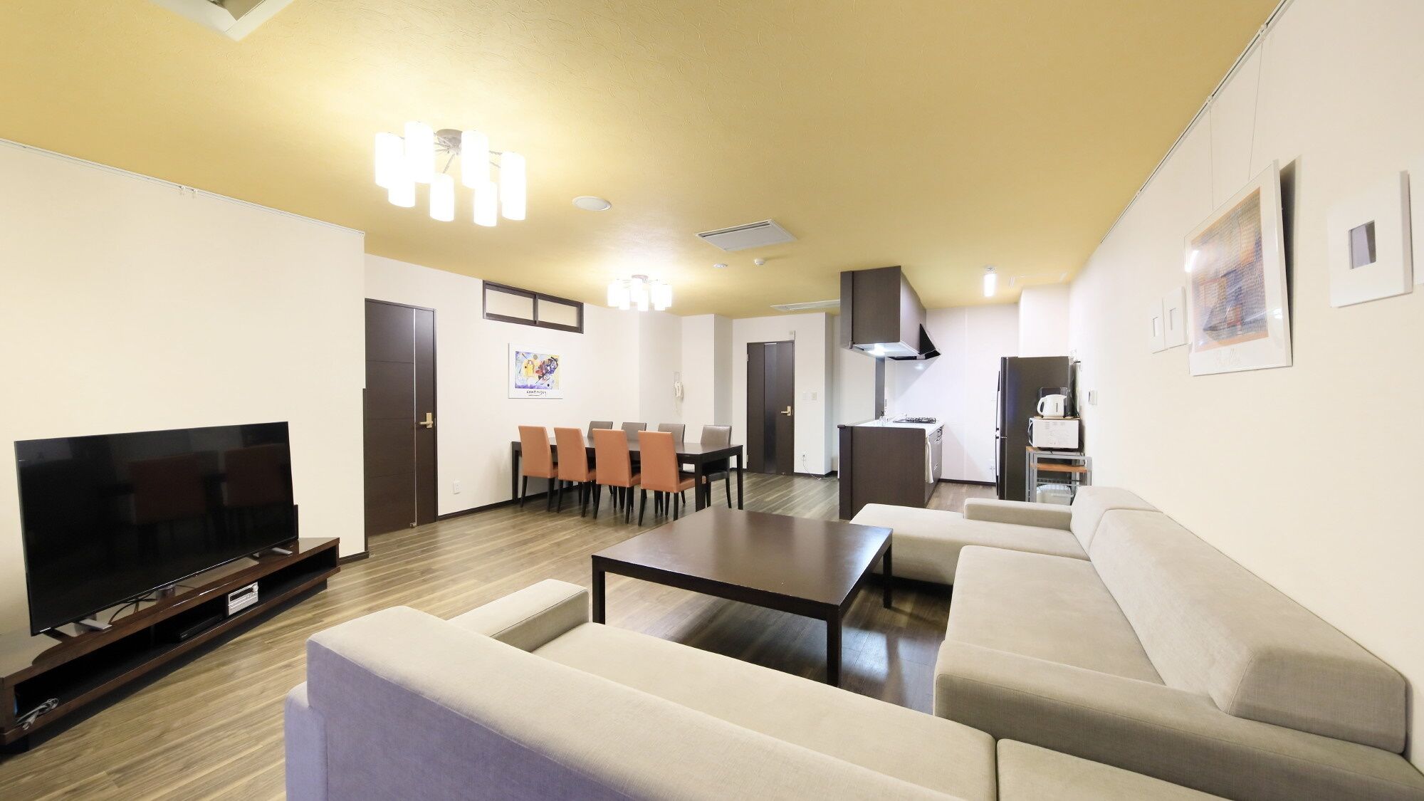 A living room with a TV, sofa, coffee table, dining table with chairs, kitchen area, and a hallway.