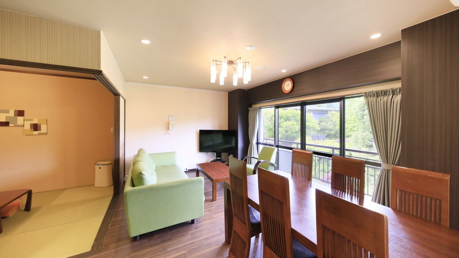 A modern living room with a sofa, dining table, chairs, a TV, and a large window with curtains.