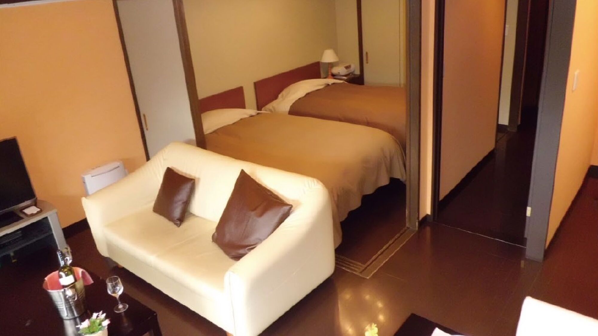 A hotel room with a single bed, a sofa, a TV, and a minibar.