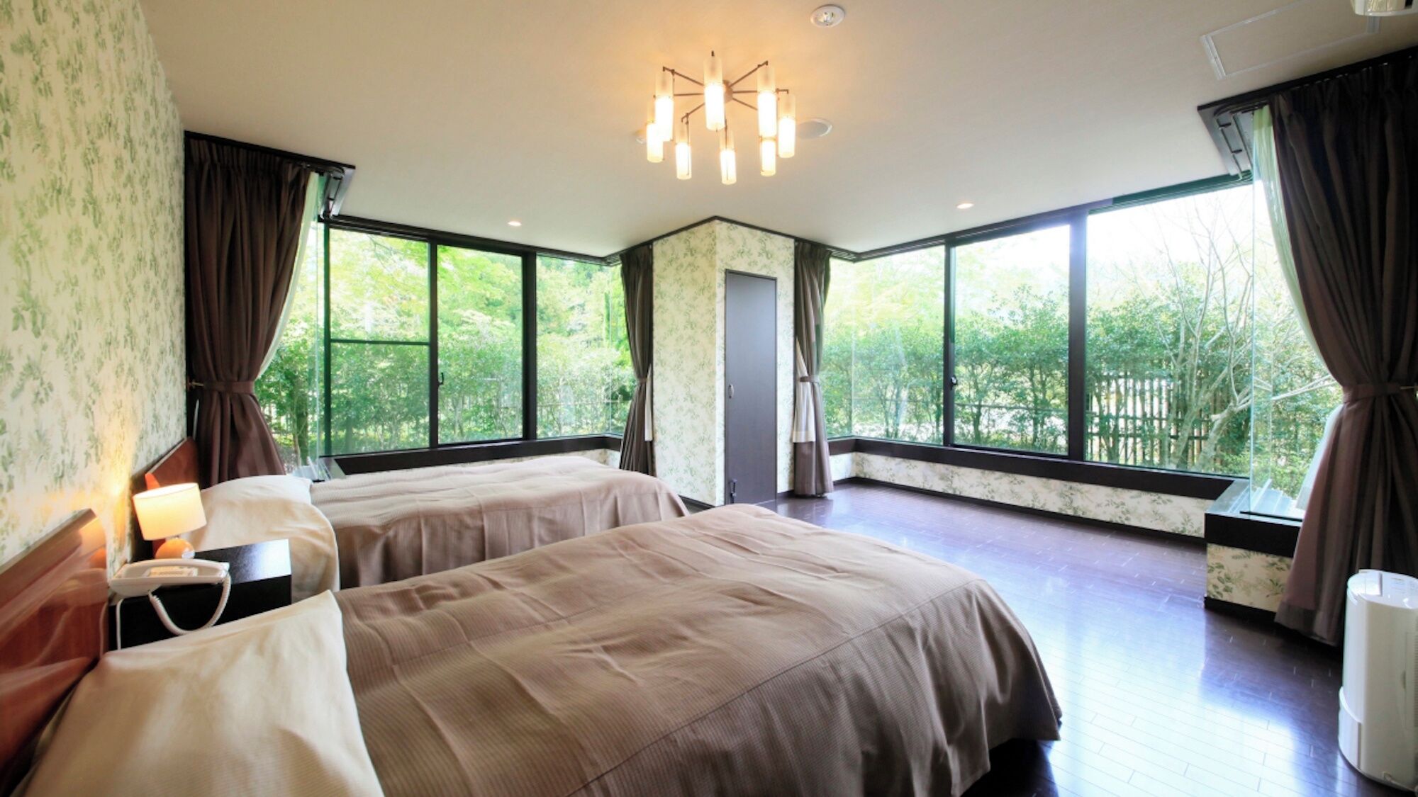 A hotel room with two beds, large windows, a chandelier, and a view of greenery outside.