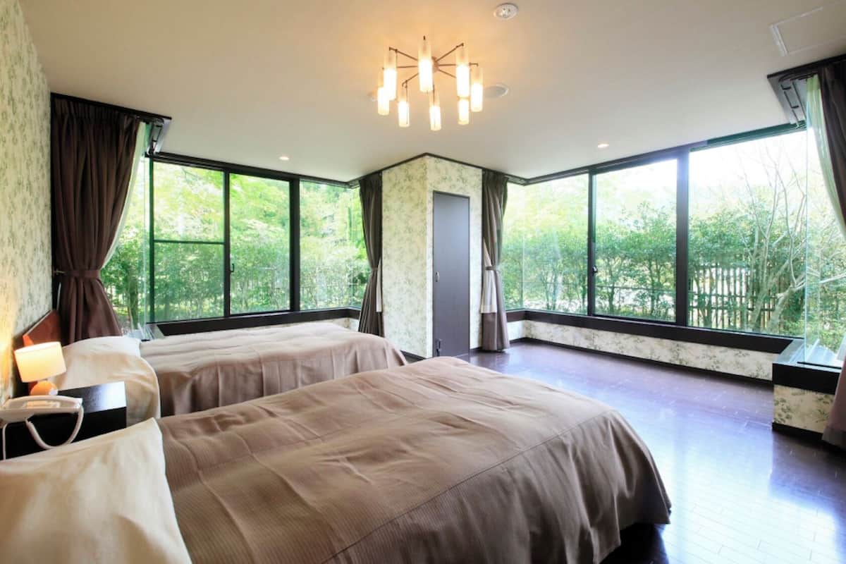 Une chambre d’hôtel avec deux lits, de grandes fenêtres, un lustre et une vue sur la verdure environnante.