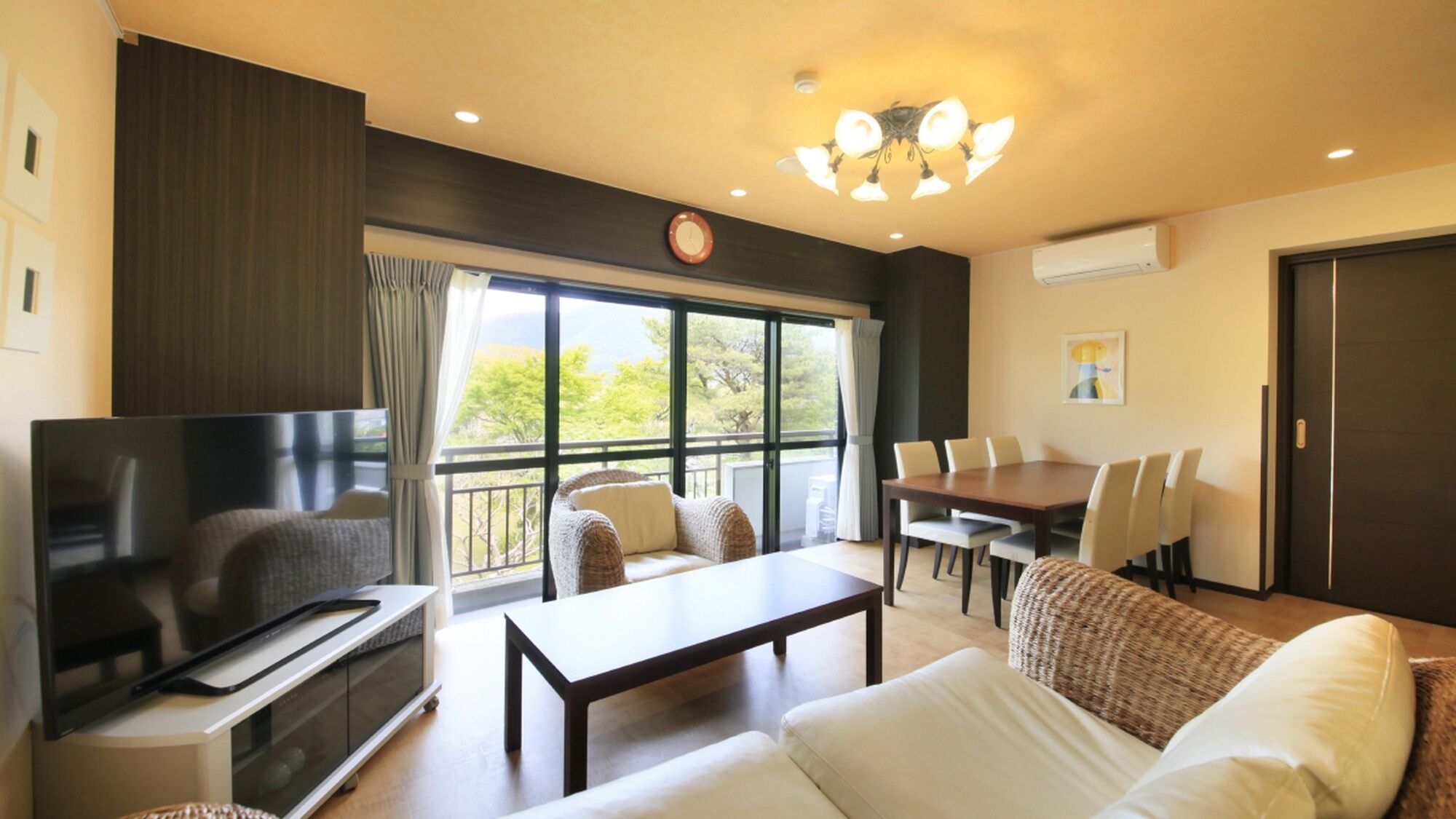 A living room with a TV, sofa, coffee table, dining table, chairs, and a balcony with a view.