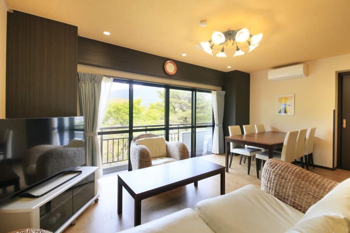 A living room with a TV, sofa, coffee table, dining table, chairs, and a balcony with a view.