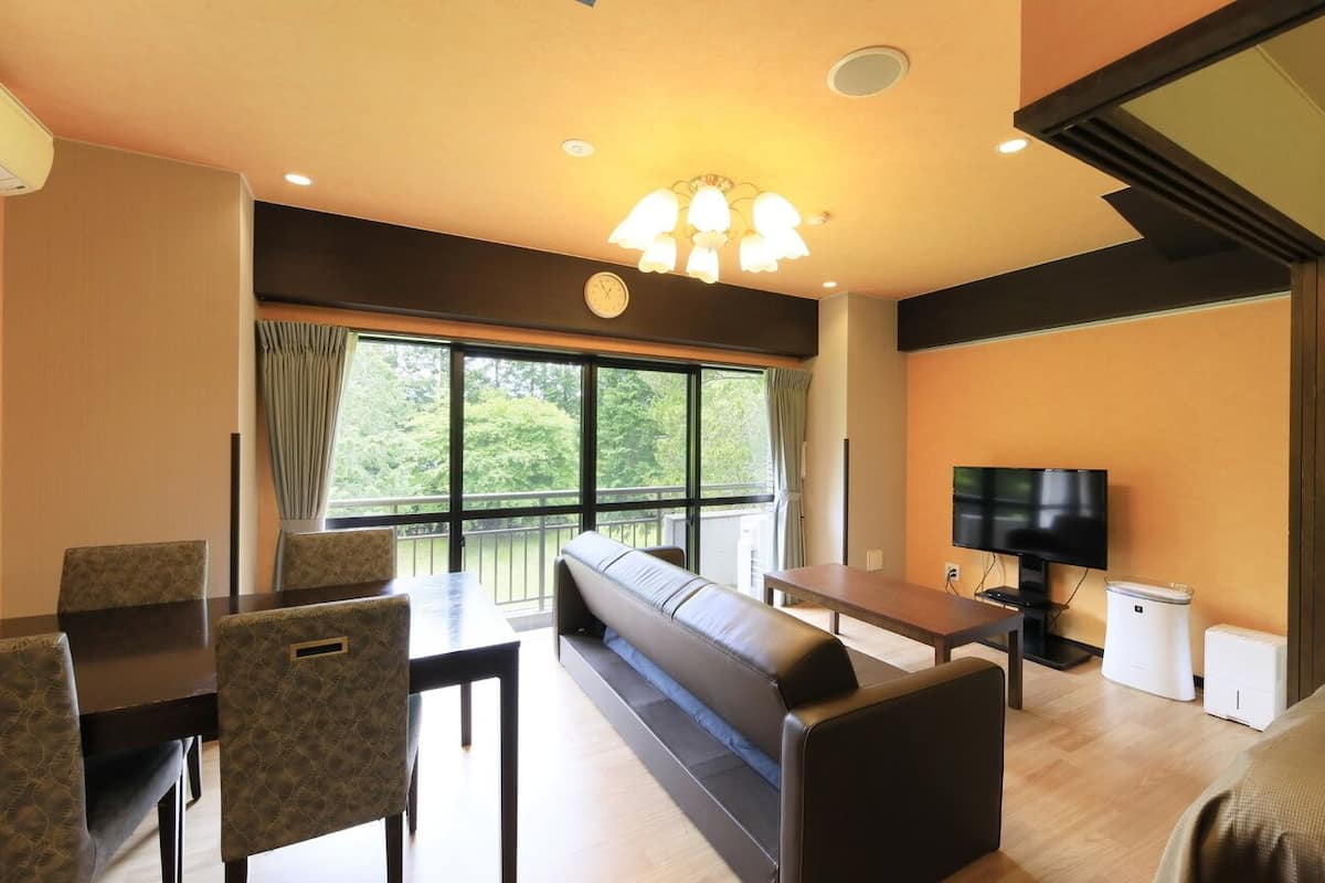 Une chambre d’hôtel comprenant un coin repas, un canapé, une télévision et une fenêtre donnant sur un espace verdoyant.