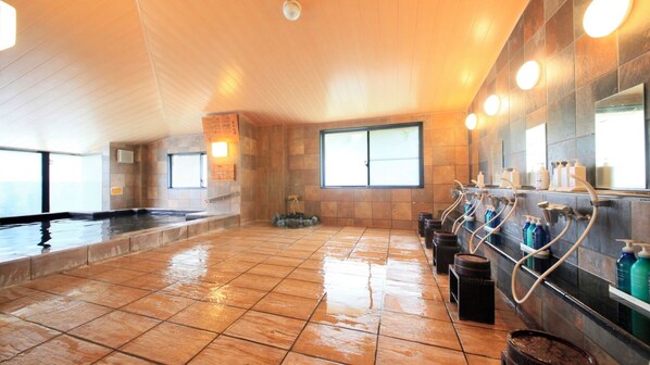 Uma piscina interior ampla com chão em mosaico, área de sauna e um dispensador de água fixado na parede.