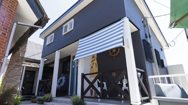 A building with a dark facade, a striped awning, and a wheel symbol. - Goto Guesthouse Sakiyama Hills (Goto)