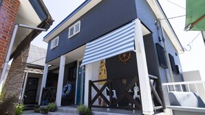 A building with a dark facade, white columns, a striped awning, and a ship wheel decoration. - Goto Guesthouse Sakiyama Hills (Goto)