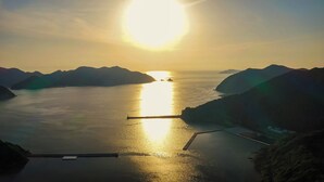 A coastal landscape with a calm sea, distant mountains, and a clear sky. - Goto Guesthouse Sakiyama Hills (Goto)