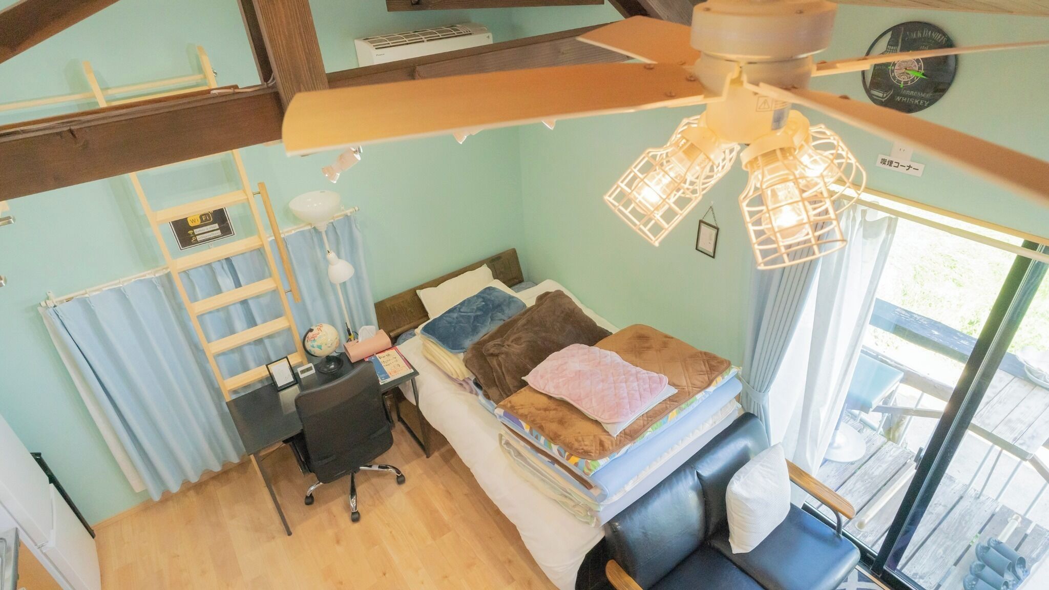 A room with a bed, desk, chair, and a ceiling fan.