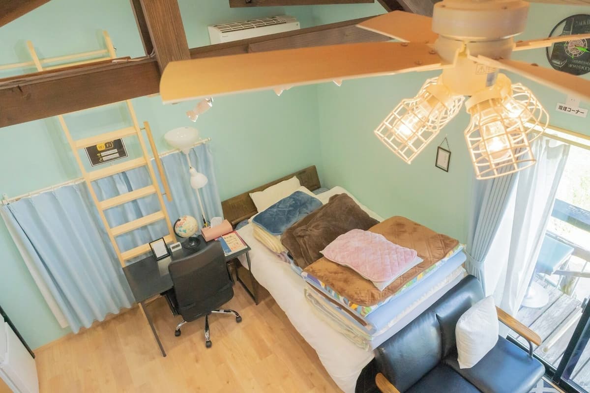 A room with a bed, desk, chair, and a ceiling fan.