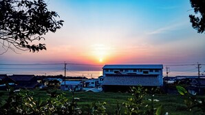 A building with a flat roof, surrounded by greenery and power lines, with a sunset in the background. - Goto Guesthouse Sakiyama Hills (Goto)