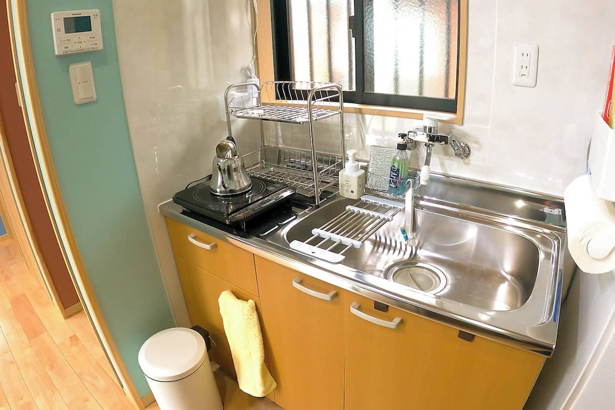 A compact kitchen with a sink, a stove, a microwave, and a small trash bin.
