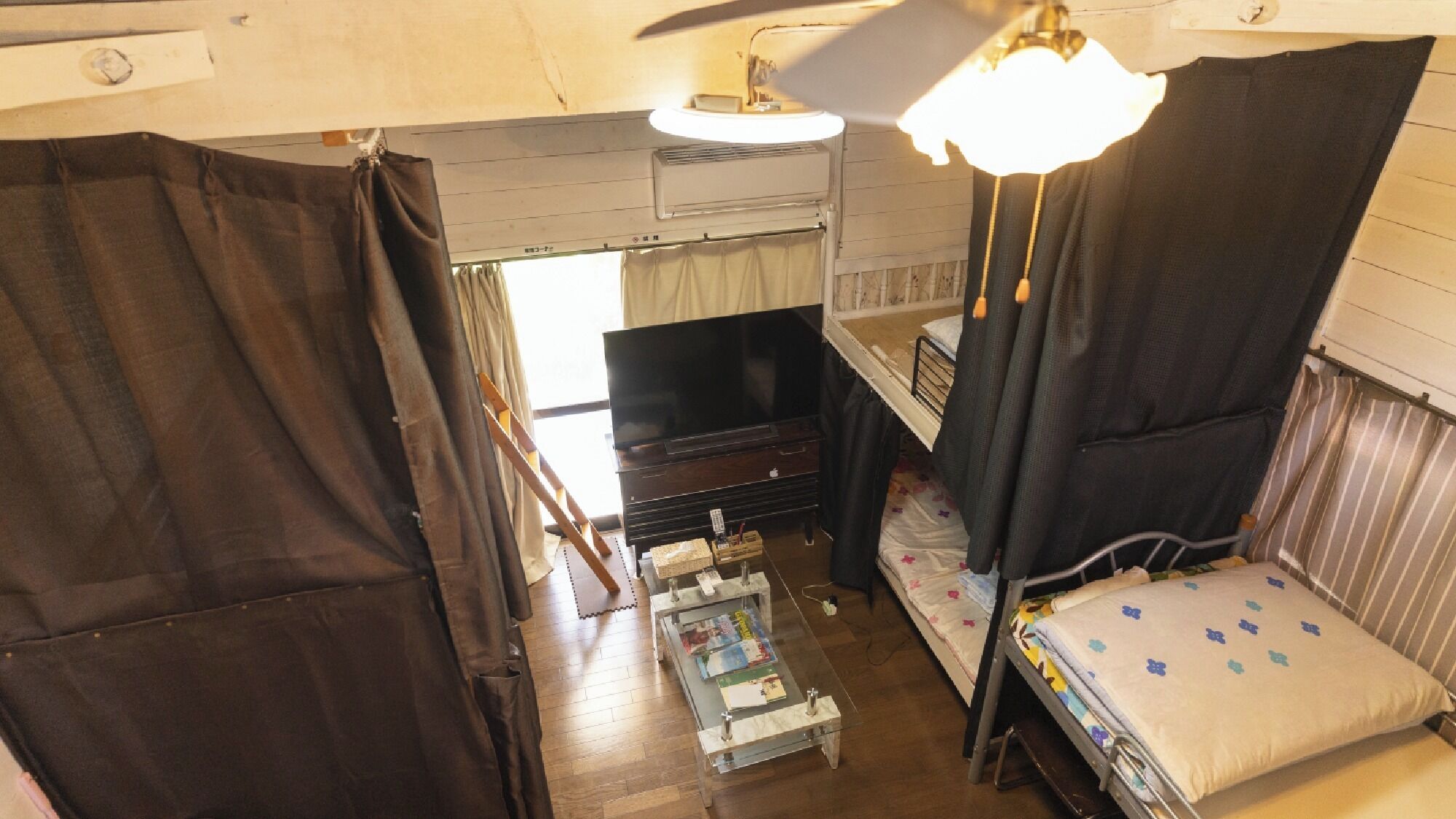 A compact room with a bed, a small table, a television, and a ceiling fan.