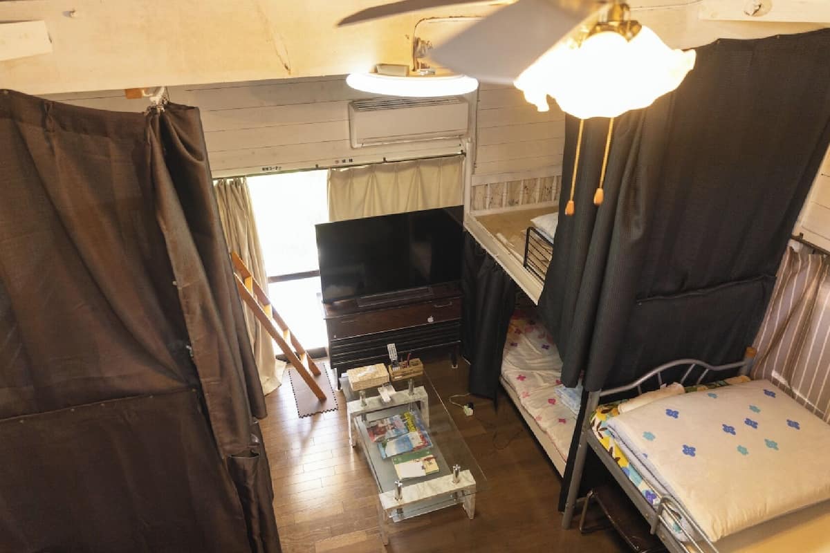 A compact room with a bed, a small table, a television, and a ceiling fan.