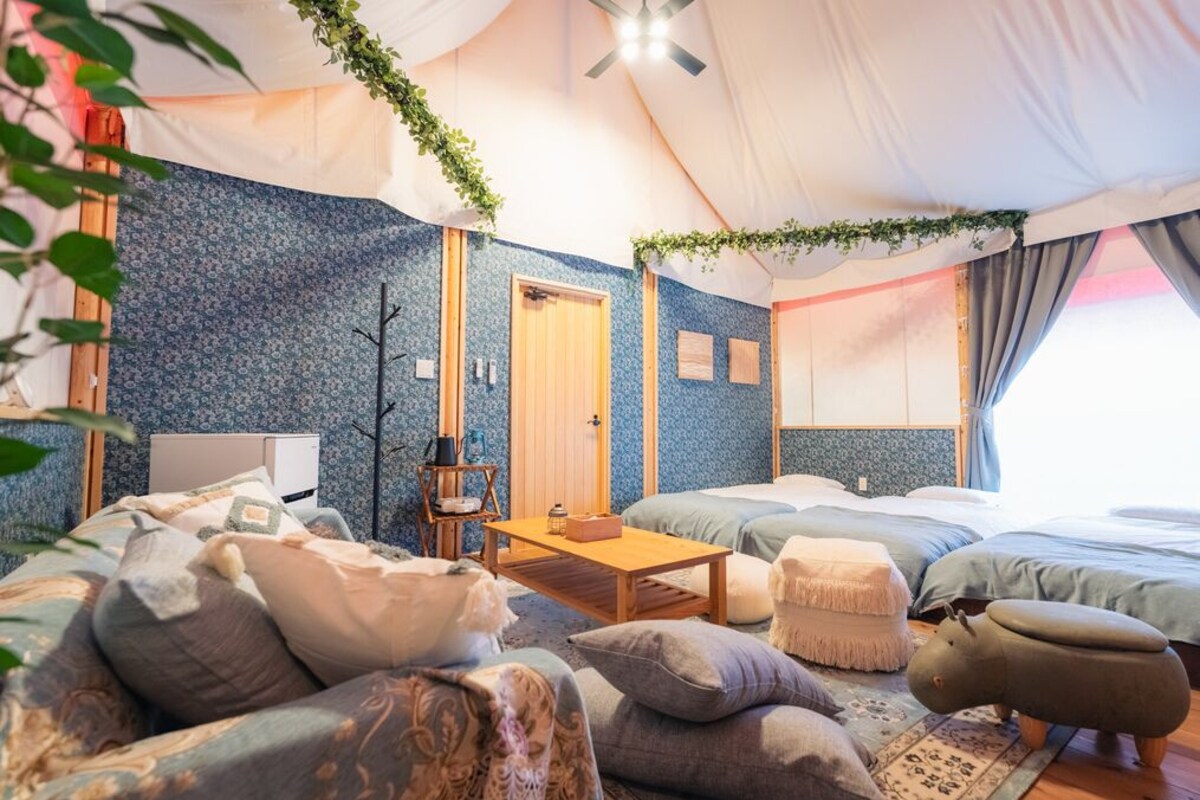 A tented accommodation with two beds, a small table, and a sofa.