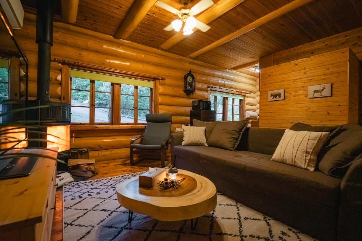 A cozy log cabin interior with a fireplace, a sofa, a chair, and a round wooden coffee table.