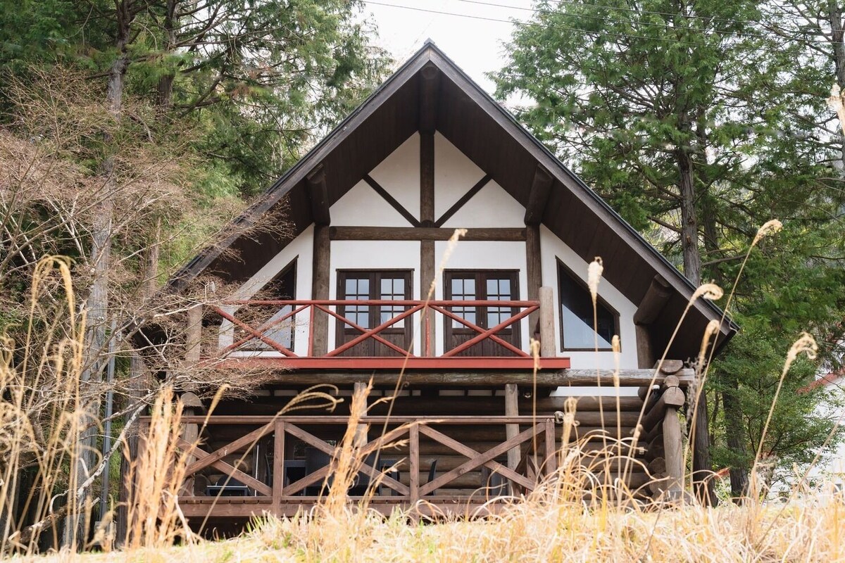 A log cabin with a balcony, surrounded by tall grass and trees.