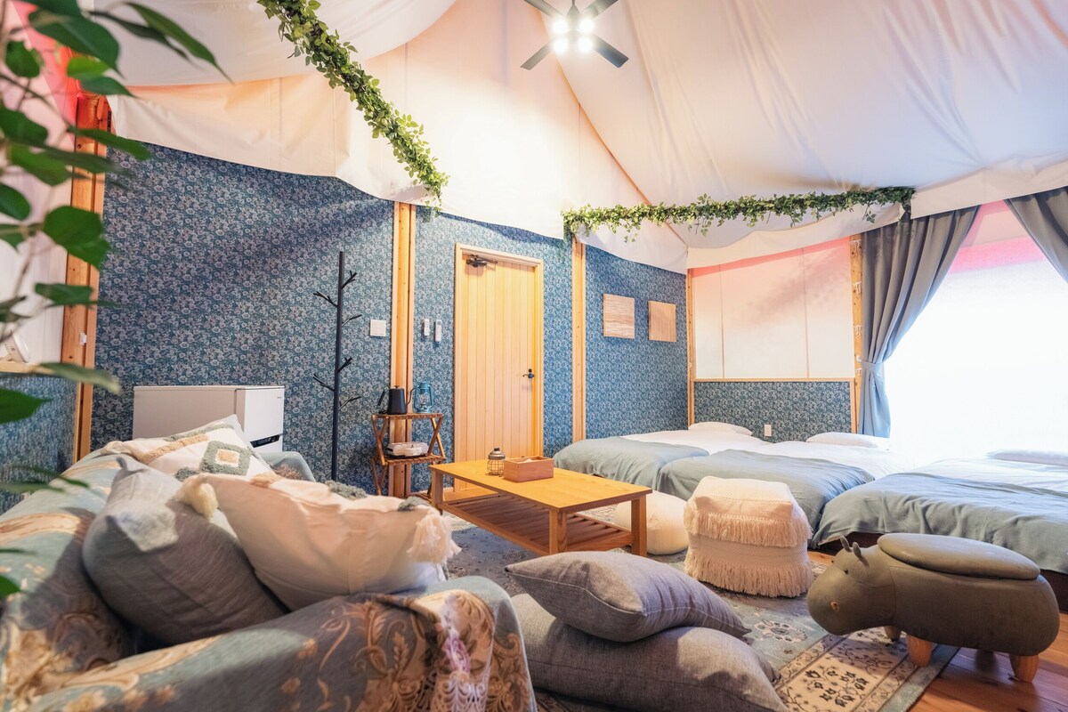 A tented accommodation with two beds, a wooden table, and a sofa.
