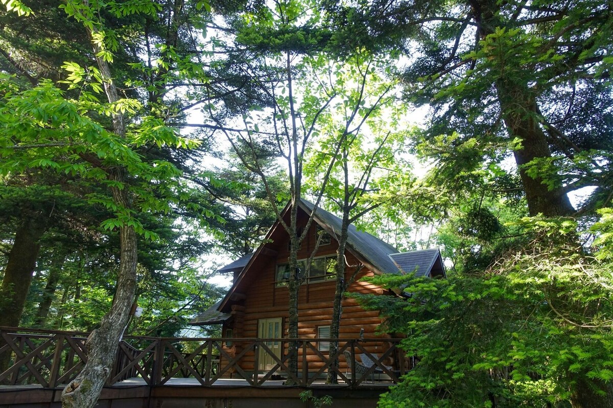 A log cabin with a sloped roof, surrounded by dense forest.