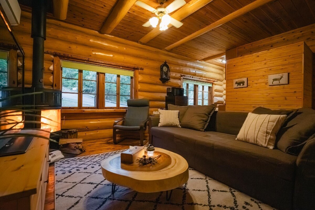 A cozy log cabin interior with a fireplace, a sofa, a chair, and a round wooden coffee table.