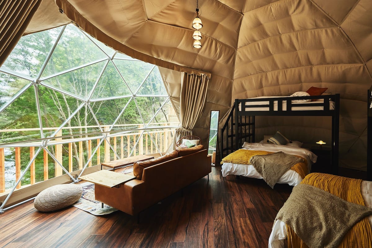 A tented room with bunk beds, a sofa, and a view of the forest.
