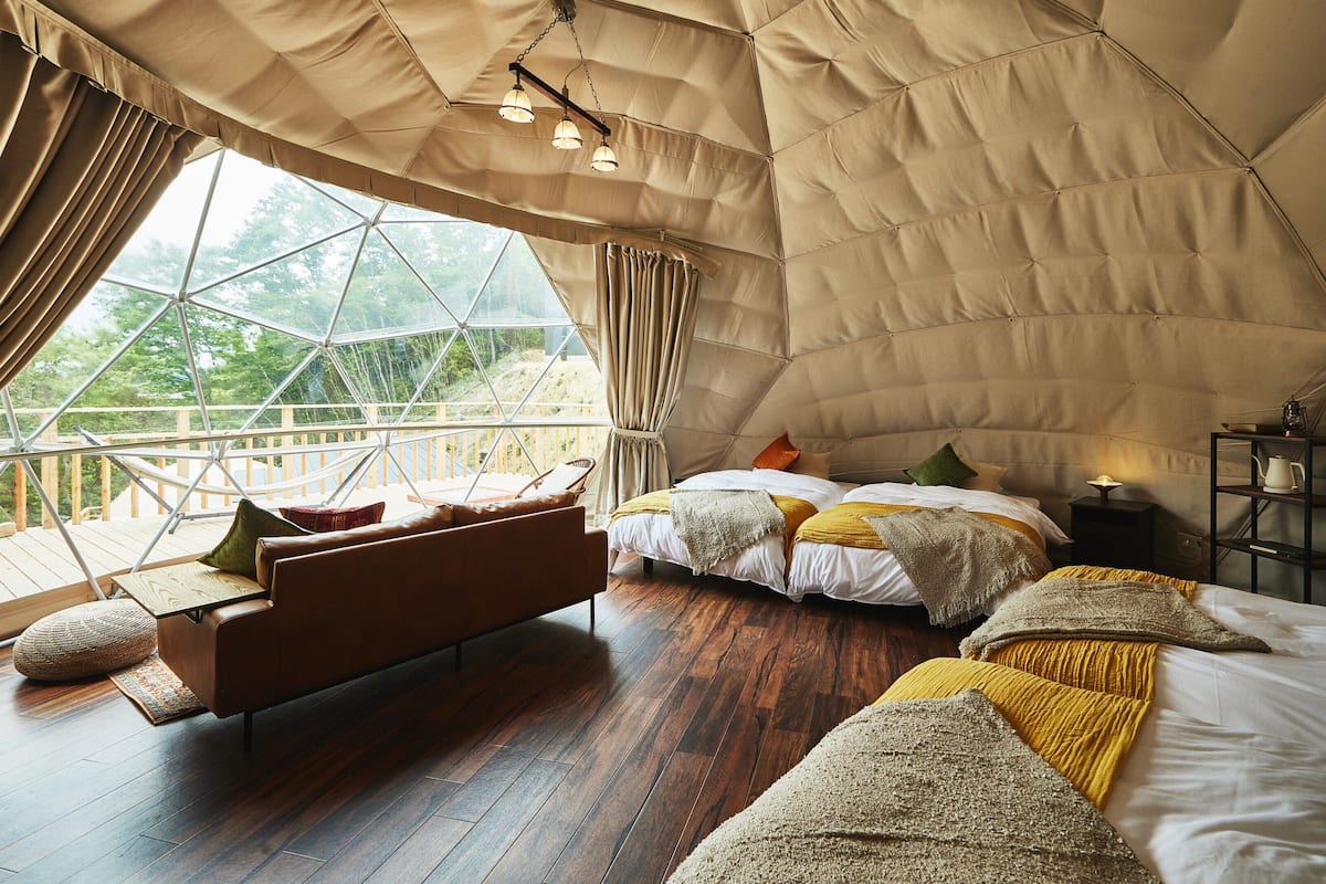 A tent-style room with a bed, seating area, and a view through a large window.