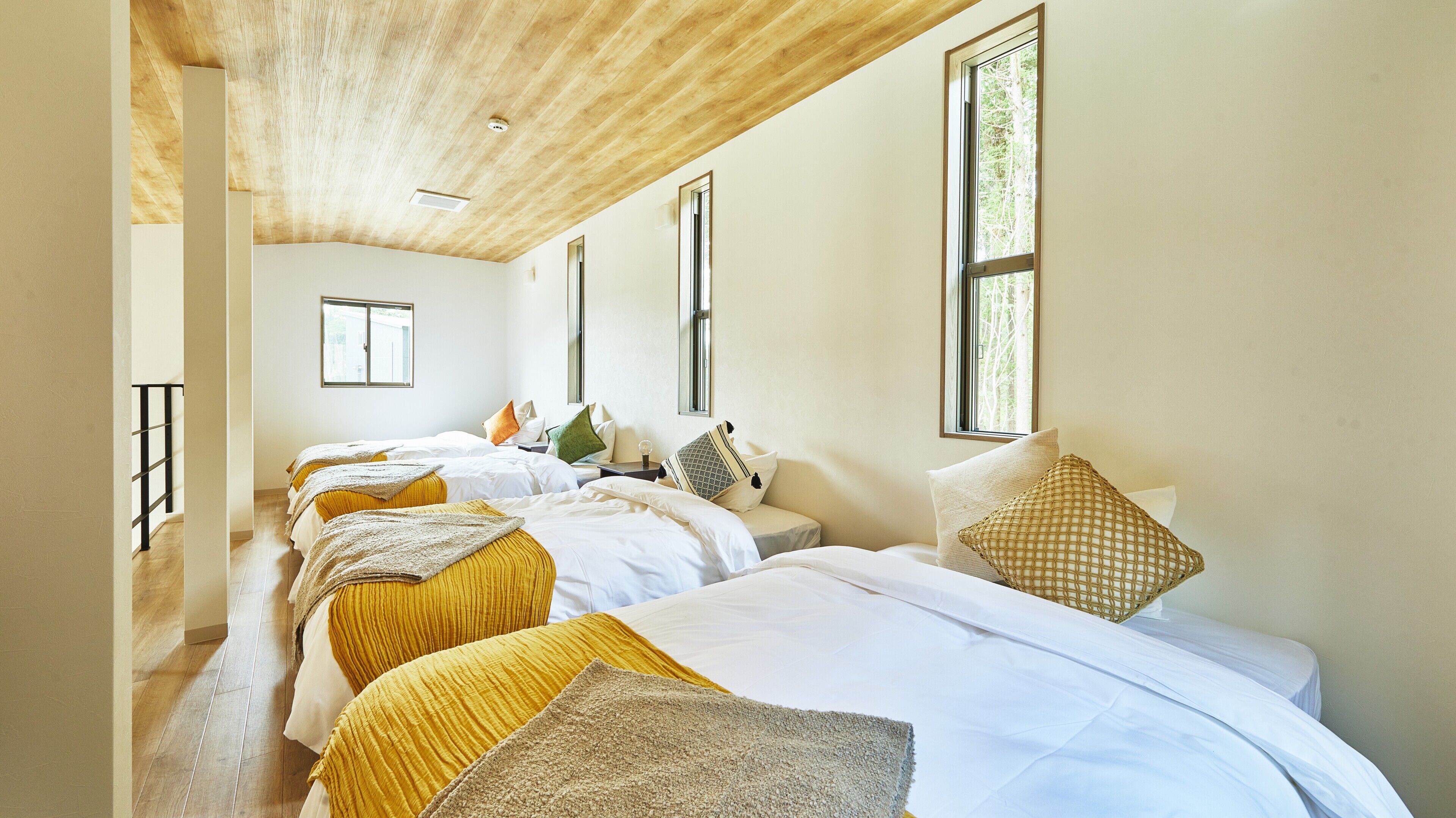 Habitación de hotel con tres camas, techo de madera, ventanas amplias y vista a árboles.