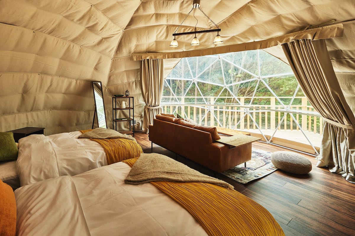 A tented accommodation with a bed, sofa, and a view of the outdoors.