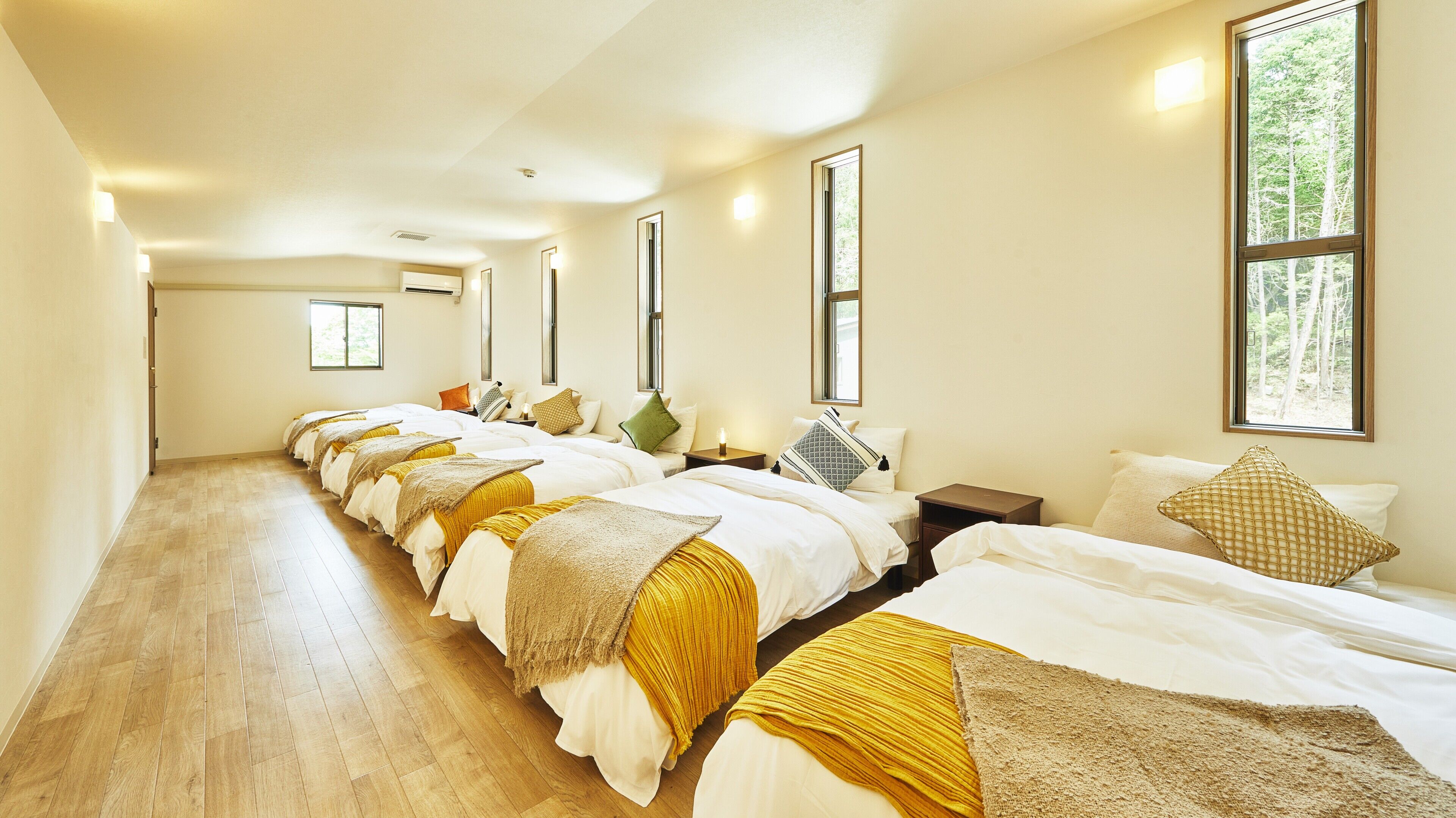 Una habitación de hotel con varias camas, suelo de madera y ventanas amplias.