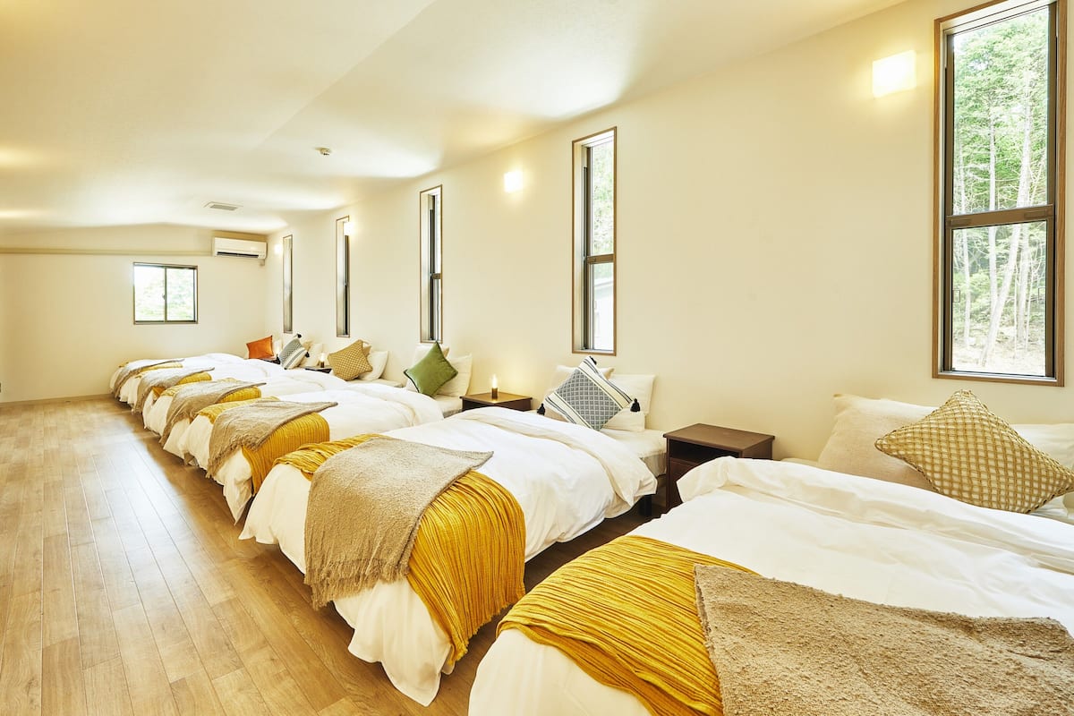 A hotel room with multiple beds, wooden flooring, and large windows.