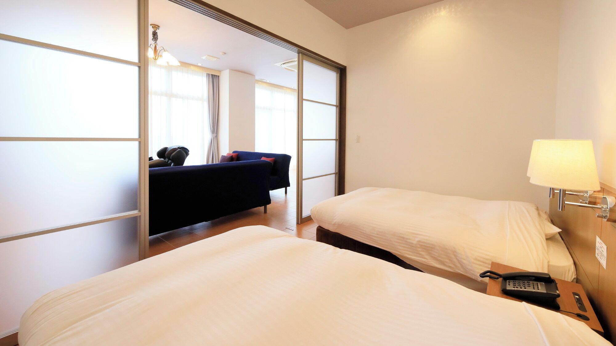 A hotel room with two beds, a sofa, a lamp, and a phone on the nightstand.