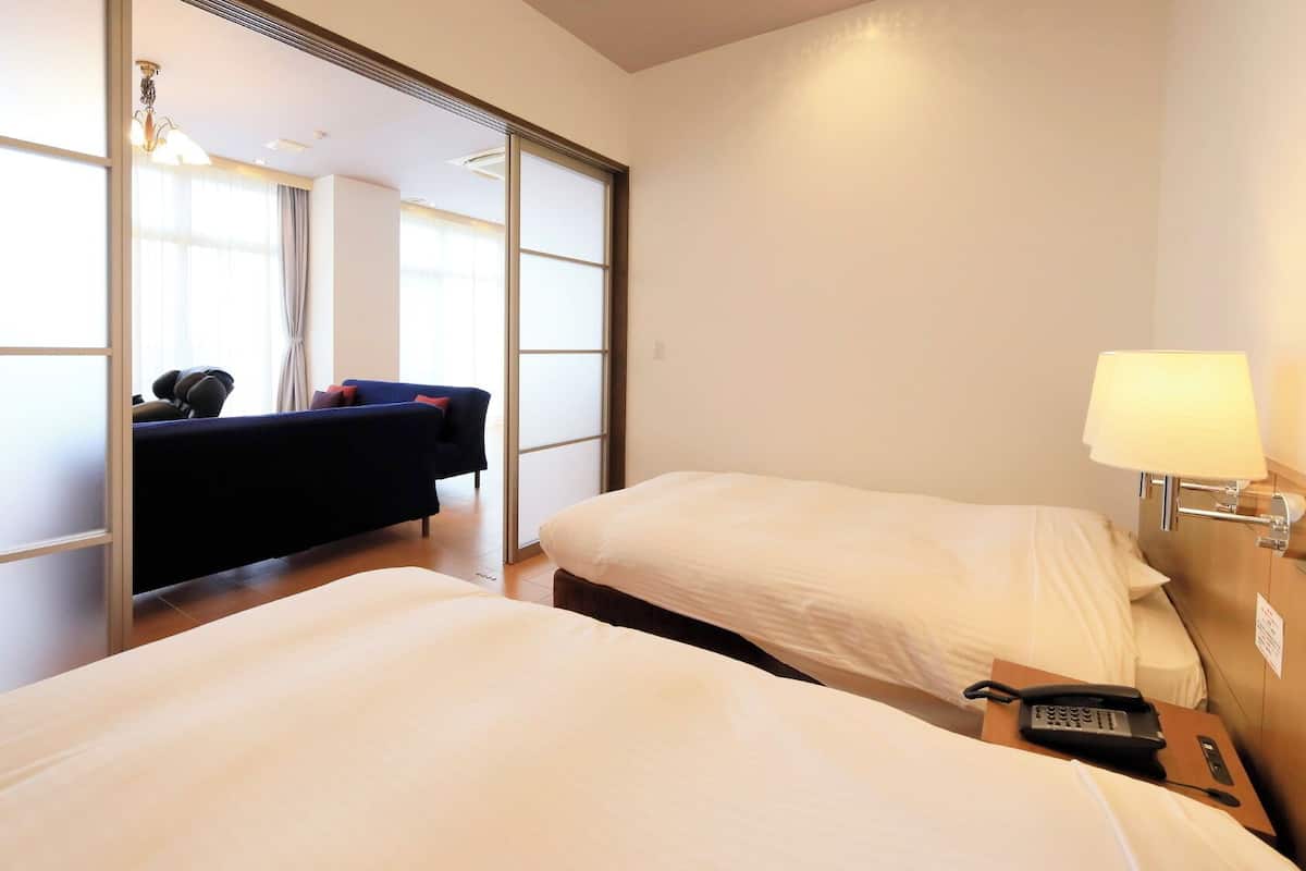Une chambre d’hôtel avec deux lits, un canapé, une lampe et un téléphone sur la table de chevet.