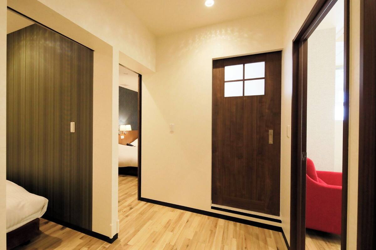 Une chambre d’hôtel avec un lit, une armoire en bois, une porte avec une fenêtre et une chaise rouge.