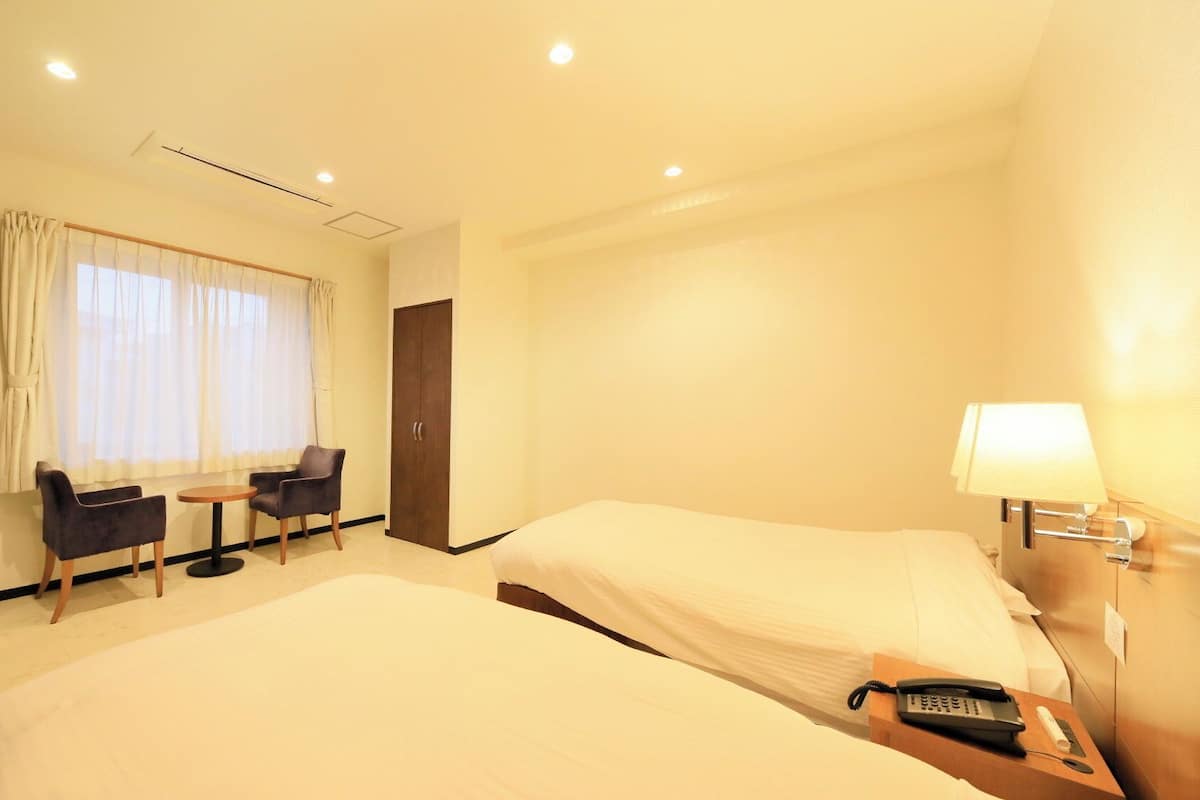 Une chambre d’hôtel avec deux lits, un bureau avec une chaise, une télévision et une lampe.