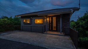 A modern house with a dark exterior, a visible garage door, and a driveway leading to the entrance. - Maigre Yebisu (Sado)