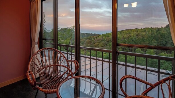 A balcony with wicker chairs and a glass table, overlooking a lush green landscape. - Maigre Yebisu (Sado)