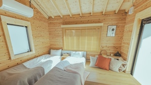 Une chambre dans un chalet en bois, avec deux lits, une fenêtre avec des stores, une petite table et une porte.