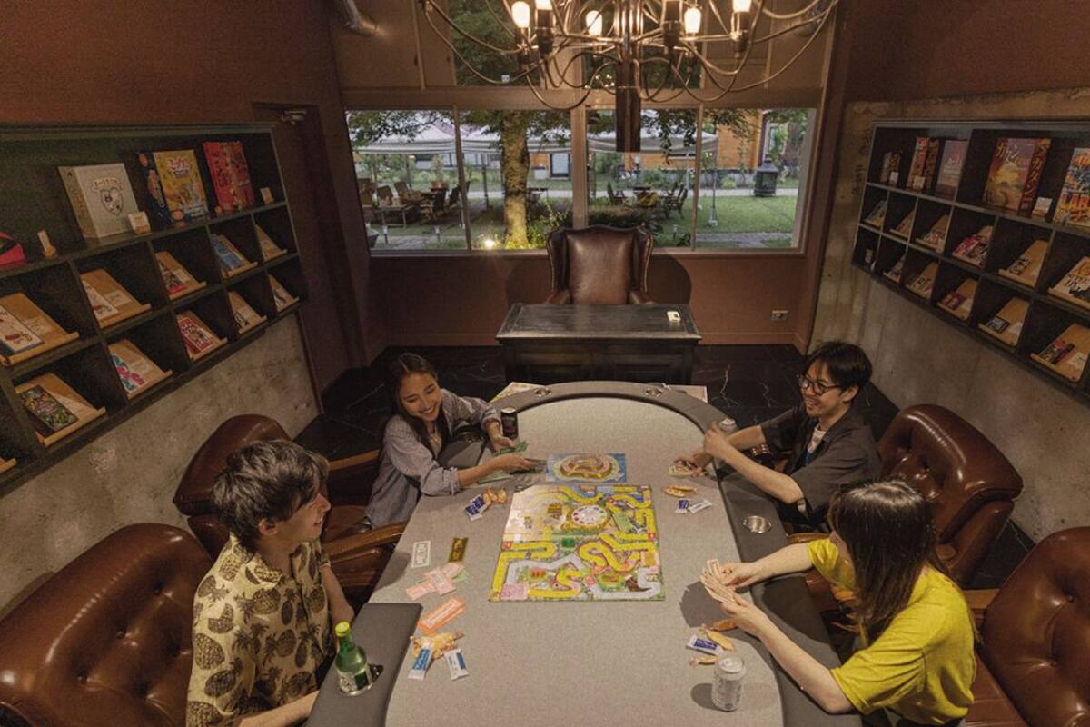 Een groep mensen speelt een spel in een kamer met lederen stoelen, een tafel en boekenkasten vol boeken.