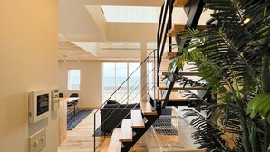Um interior moderno com uma escada, uma área de refeições e vista para o mar.