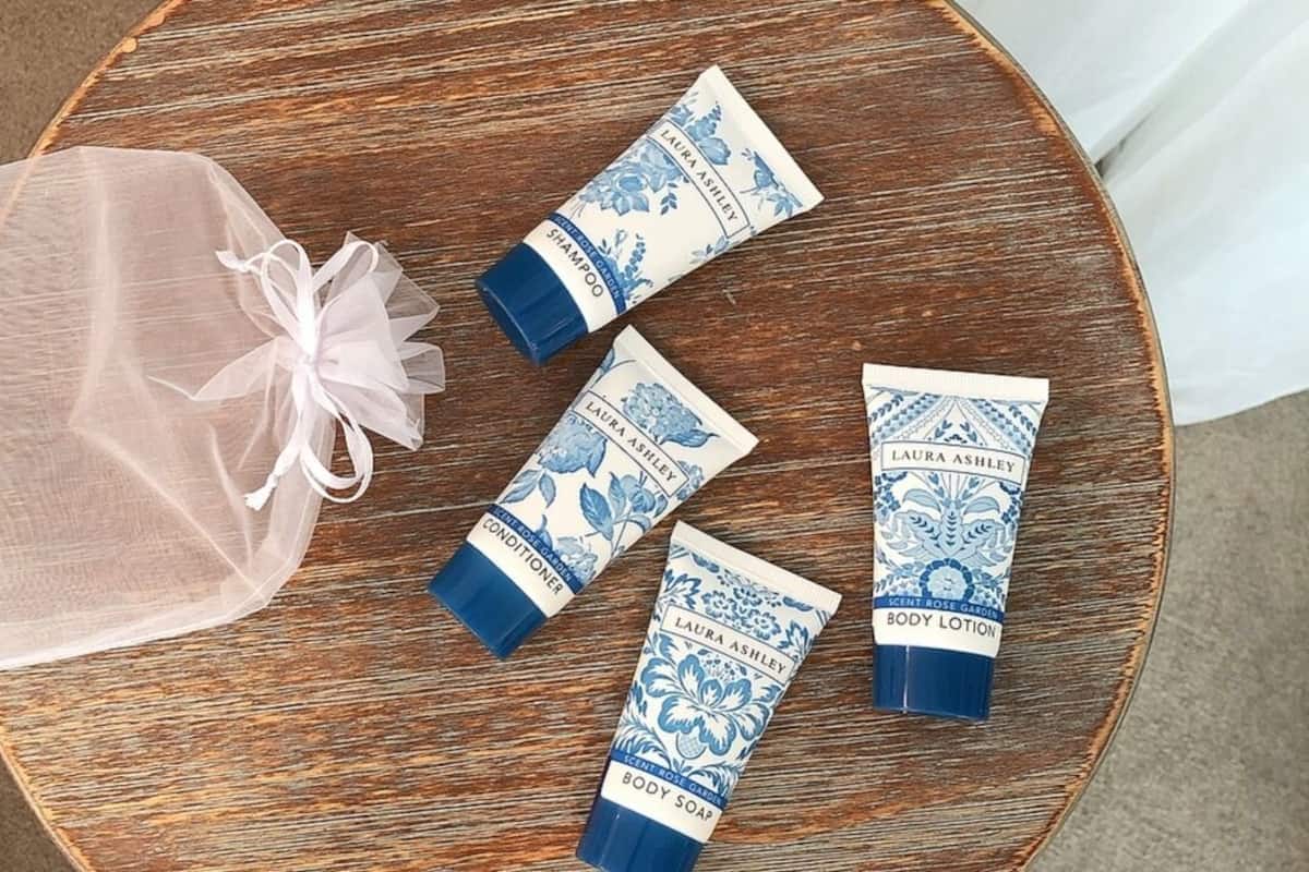 Ein runder Holztisch mit vier Körperpflegeprodukten von Laura Ashley und einer transparenten Plastiktüte.