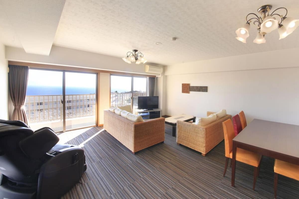 Ein Hotelzimmer mit Balkon, Fernseher, einer Couch, einem Esstisch und Stühlen.