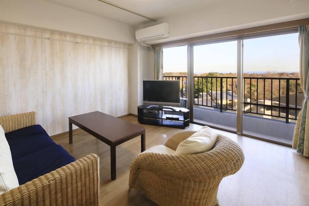 Ein Wohnzimmer mit einer Couch, zwei Sesseln, einem Couchtisch, einem Fernseher und einem Balkon mit Blick.
