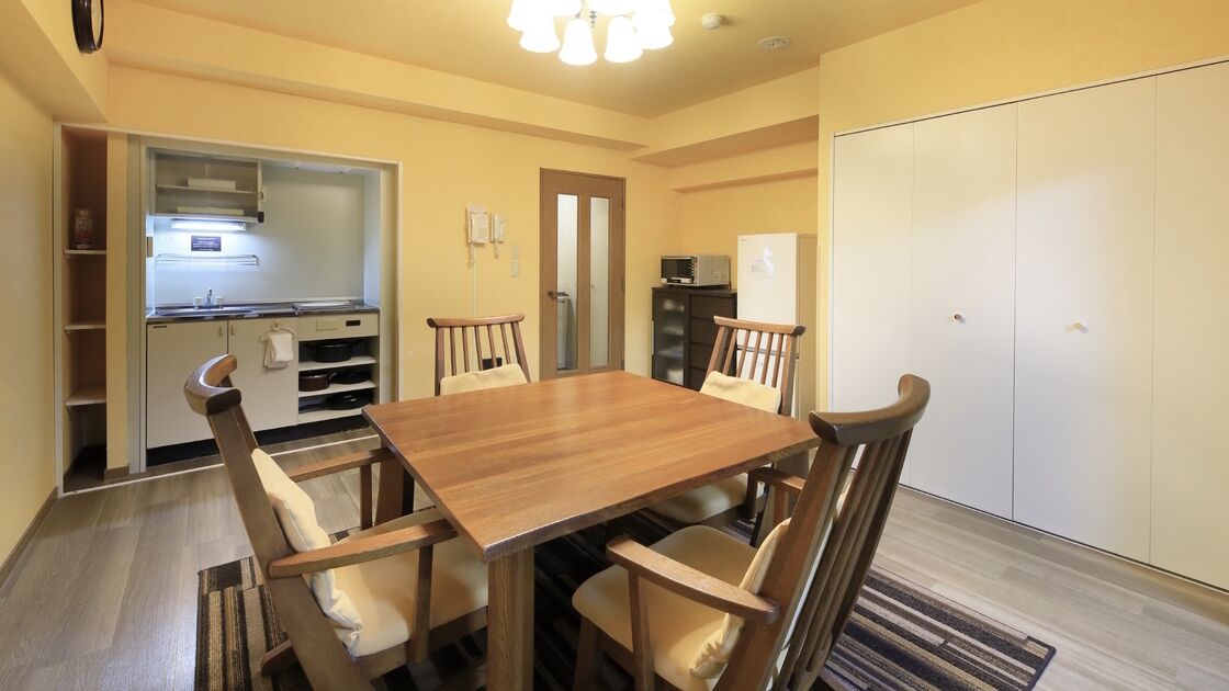A dining area with a wooden table and chairs, a kitchen with cabinets and appliances, and a wardrobe with doors.