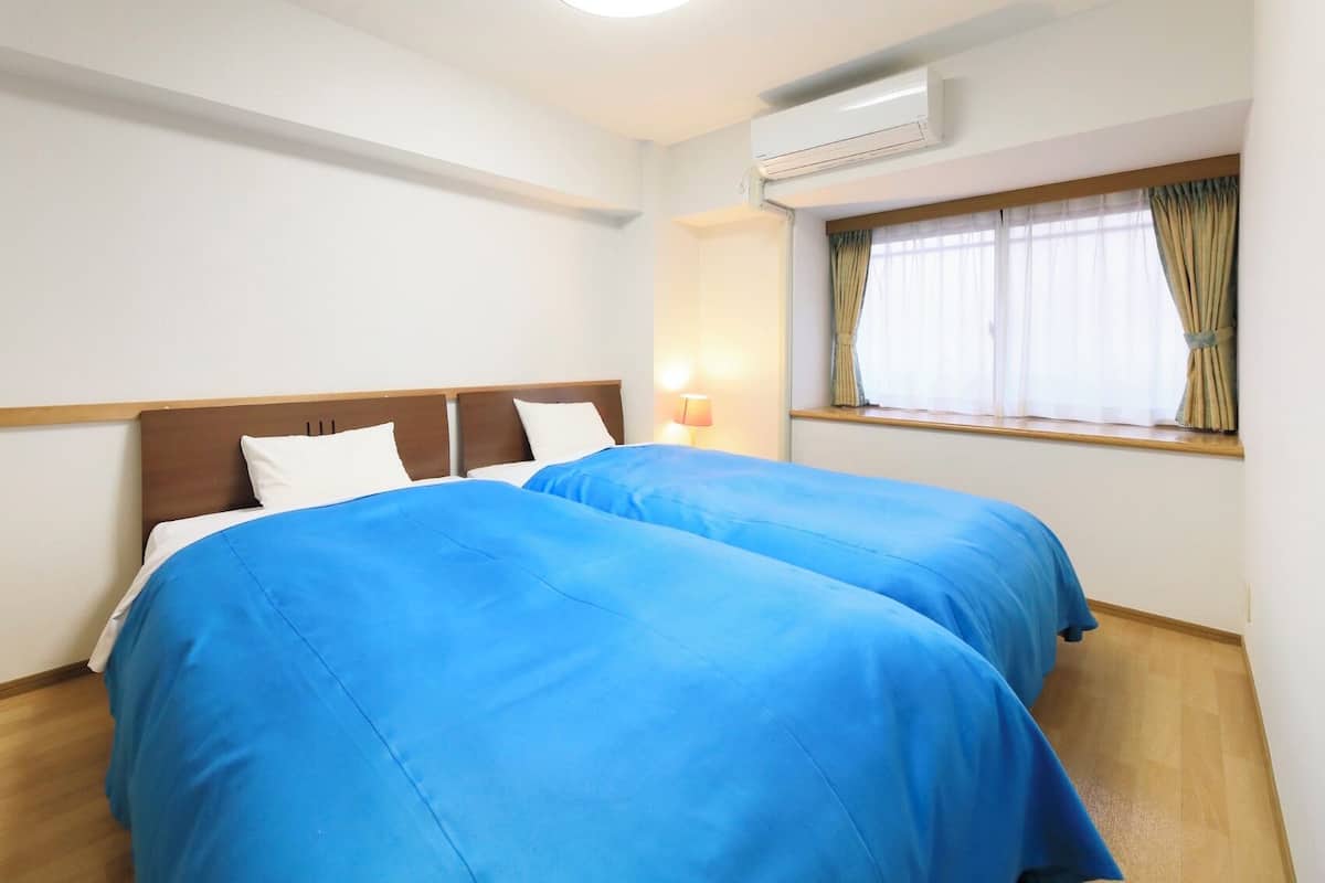 Ein Hotelzimmer mit zwei Betten, einem Vorhangfenster, einer Klimaanlage und Holzboden.