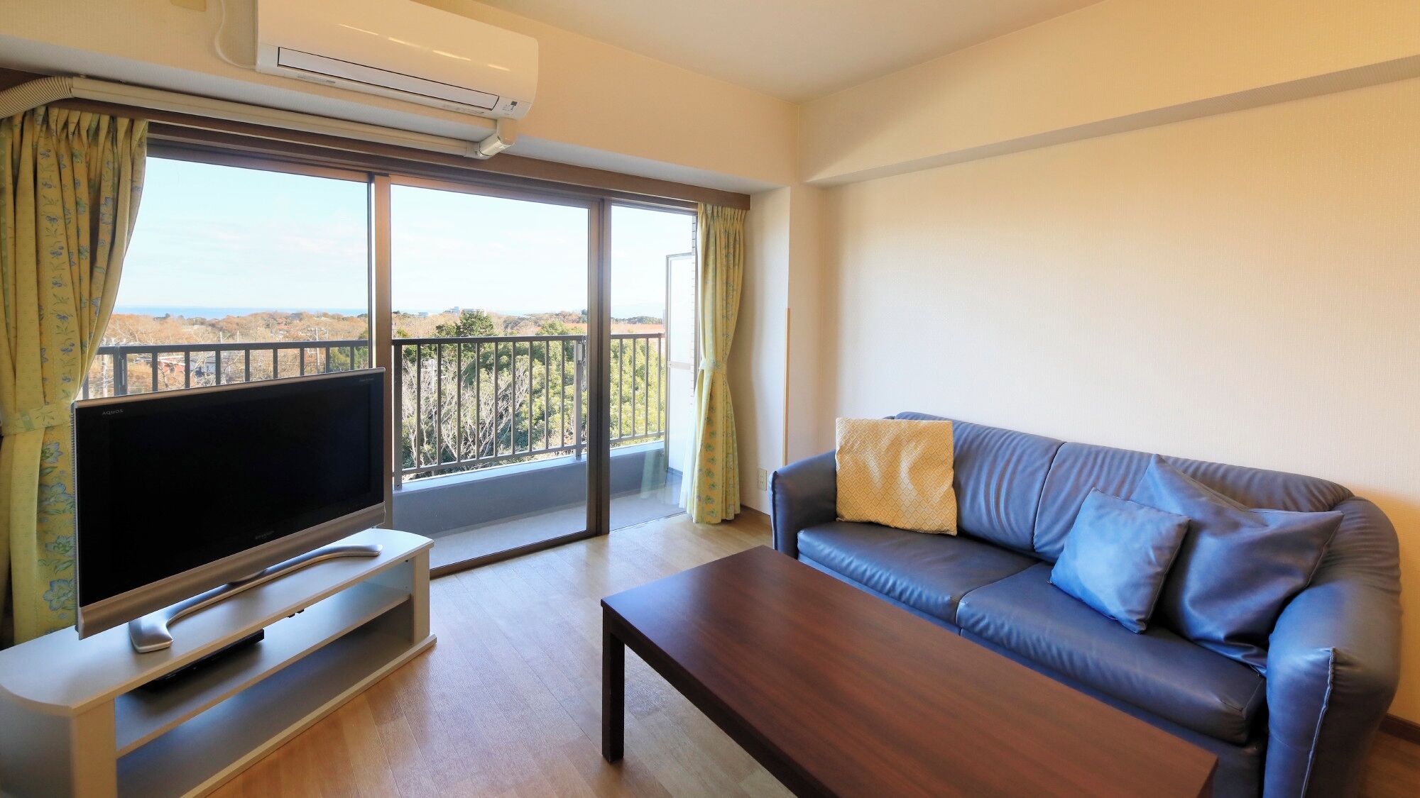 Un salón con televisor de pantalla plana, un sofá, una mesa de centro y un balcón con vistas.