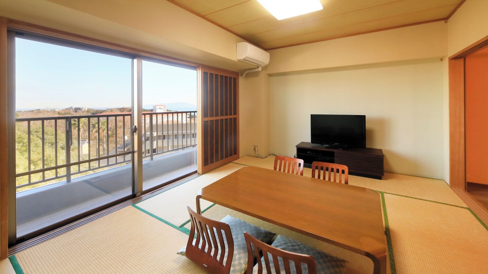 A room with tatami flooring, a sliding glass door, a television, and a dining table with chairs.
