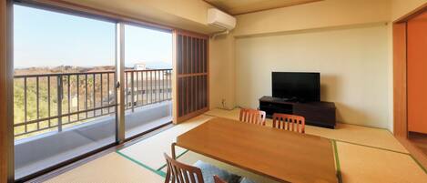 A room with tatami flooring, a sliding glass door, a television, and a dining table with chairs.