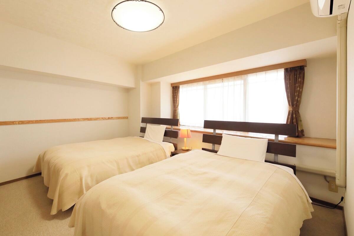 Ein Hotelzimmer mit zwei Betten, einem Fenster mit Vorhängen, einer Nachttischlampe und einer Deckenleuchte.