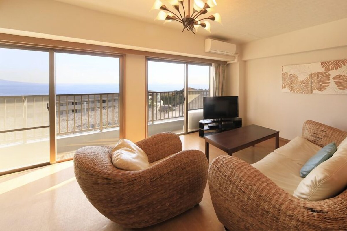 Een woonkamer met rieten meubels, een televisie en een balkon met uitzicht.