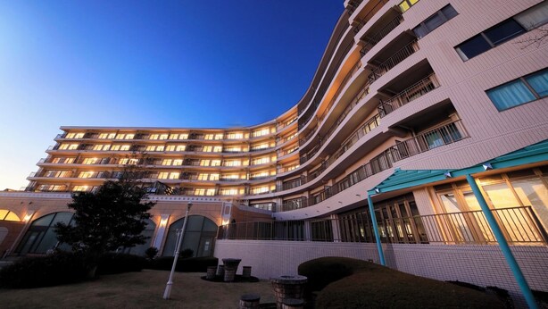 A multi-story hotel with a curved facade, balconies, and a well-lit entrance. - Point Vacation Izu Kogen (Ito)